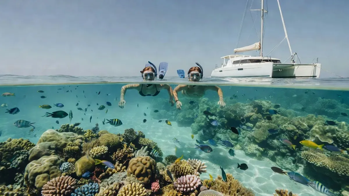 Snorkelers in the water beside a sailing catamaran over a Cozumel reef on a Playa del Carmen boat tour, Mexico