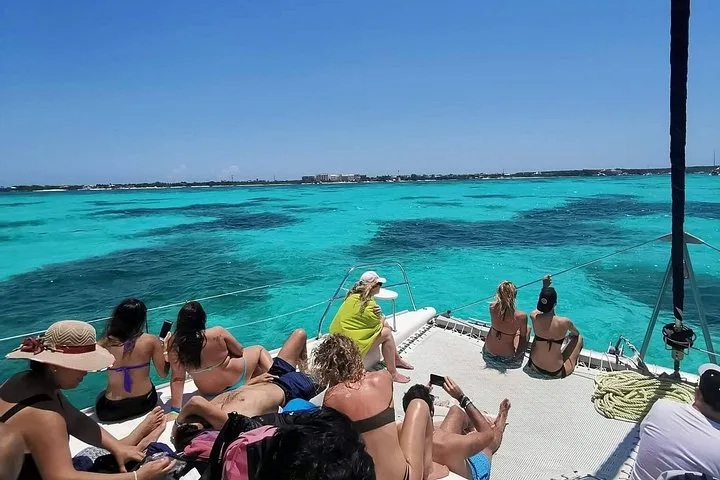 Guests on the bow nets of a catamaran over turquoise reef water on the way to Isla Mujeres, an Isla Mujeres catamaran from Playa del Carmen